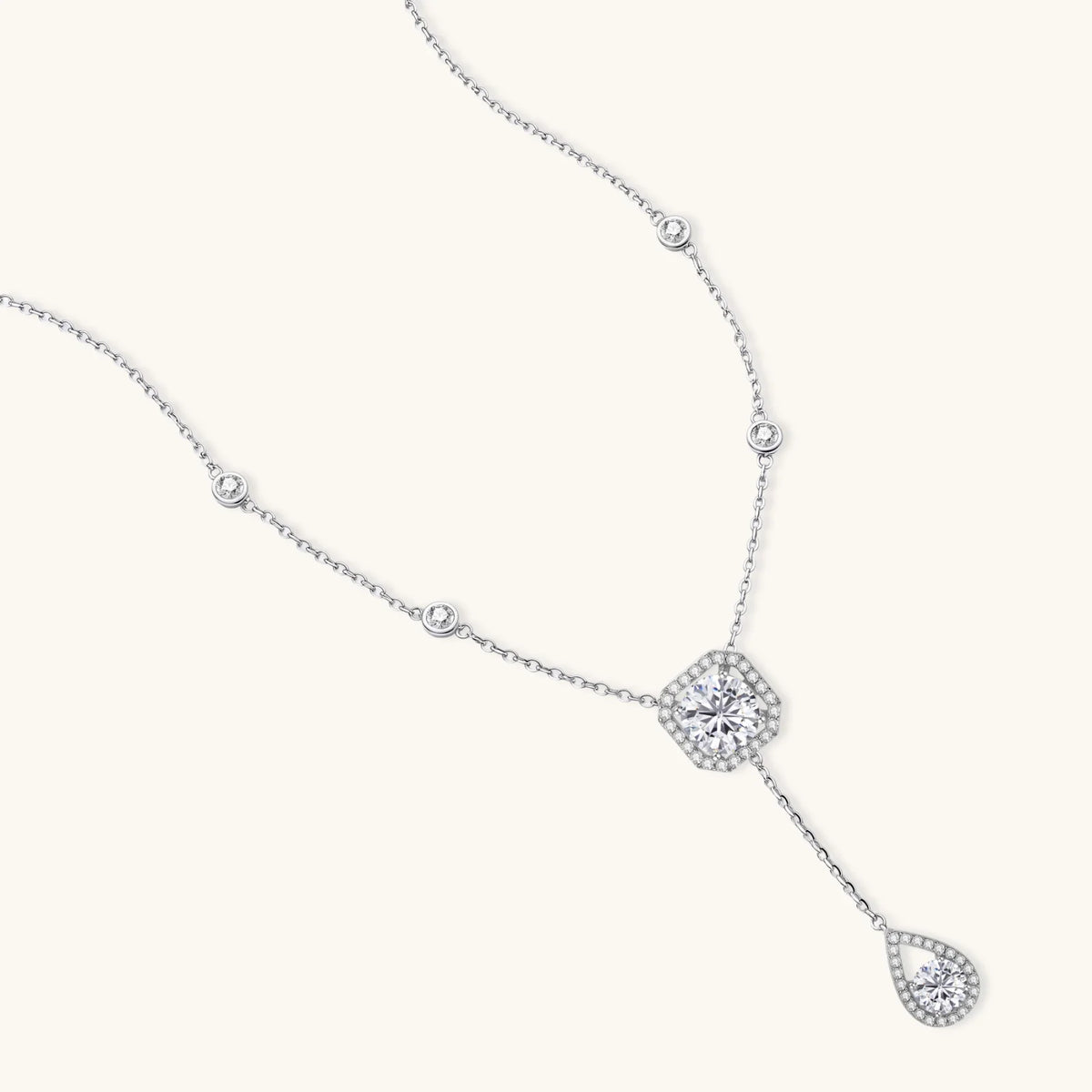 sterling silver necklace with cushion-cut moissanite in halo setting and teardrop pendant, displayed on cream background.