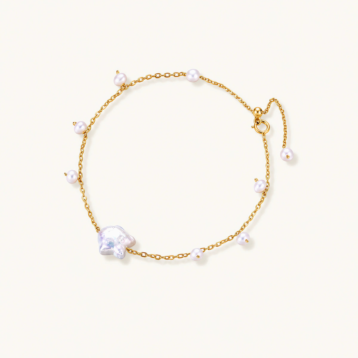 Delicate gold chain bracelet with baroque pearl centerpiece and small freshwater pearls on cream background.