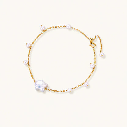 Delicate gold chain bracelet with baroque pearl centerpiece and small freshwater pearls on cream background.