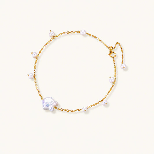 Delicate gold chain bracelet with baroque pearl centerpiece and small freshwater pearls on cream background.