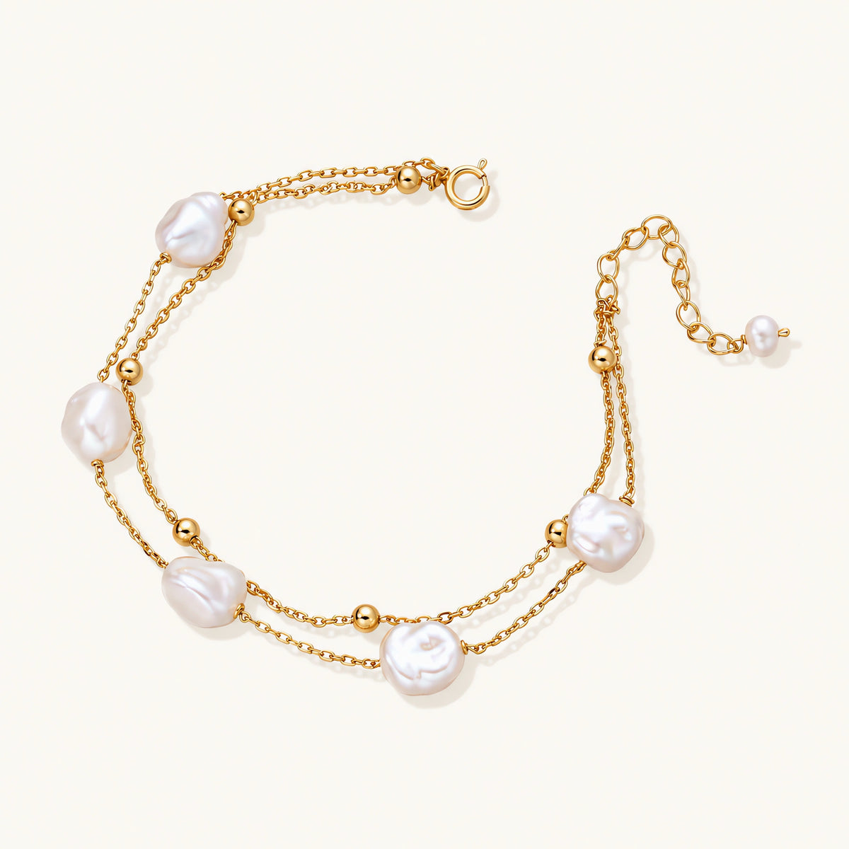 double-strand gold bracelet with irregular baroque pearls and smooth freshwater pearls on cream background.