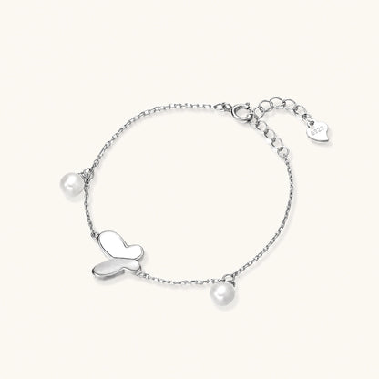 Delicate rhodium-plated silver chain bracelet with butterfly charm and two freshwater pearls on cream background