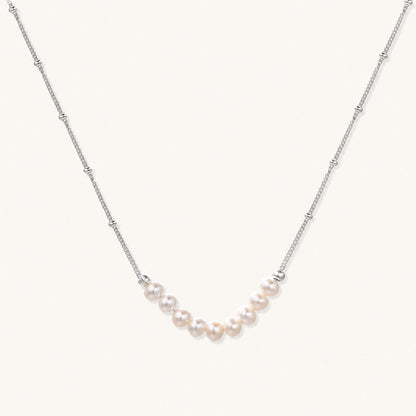 Delicate sterling silver chain necklace with small freshwater pearls arranged in a curved smile arc on cream background.