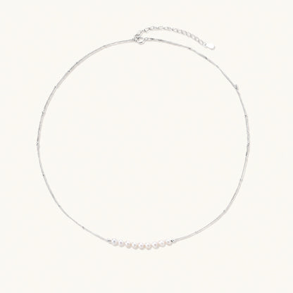 Delicate sterling silver chain necklace with small freshwater pearls arranged in a curved smile arc on cream background.