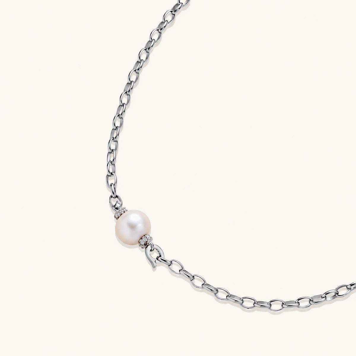 Dainty rhodium-plated silver chain necklace with centered 10mm freshwater pearl and crystal accents on cream background