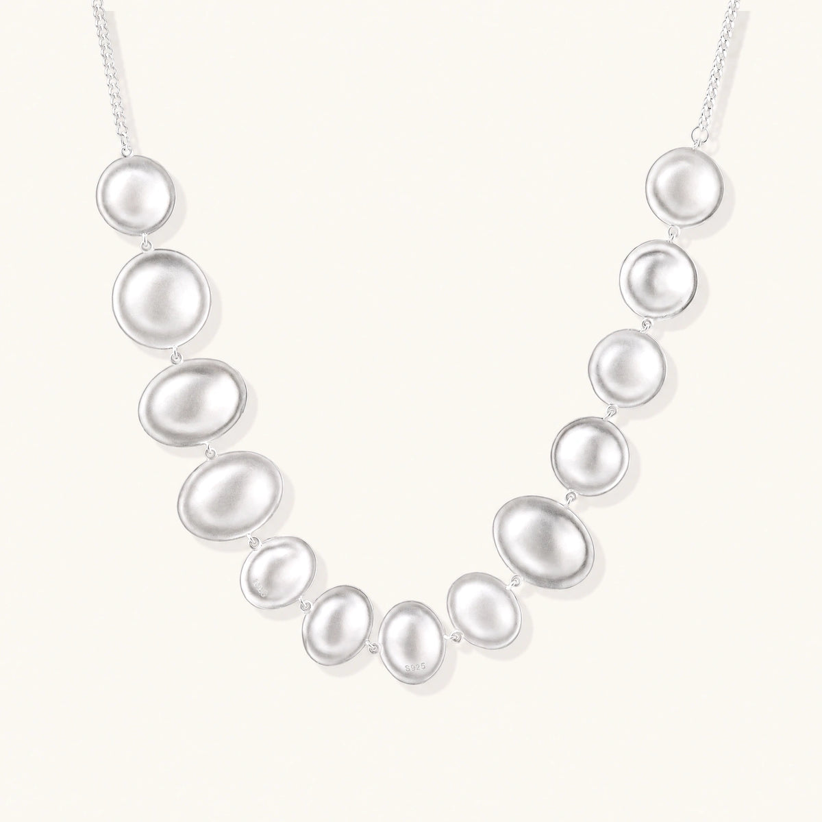 Sterling silver necklace with fourteen matte concave round and oval discs on a curb chain with an adjustable extender.