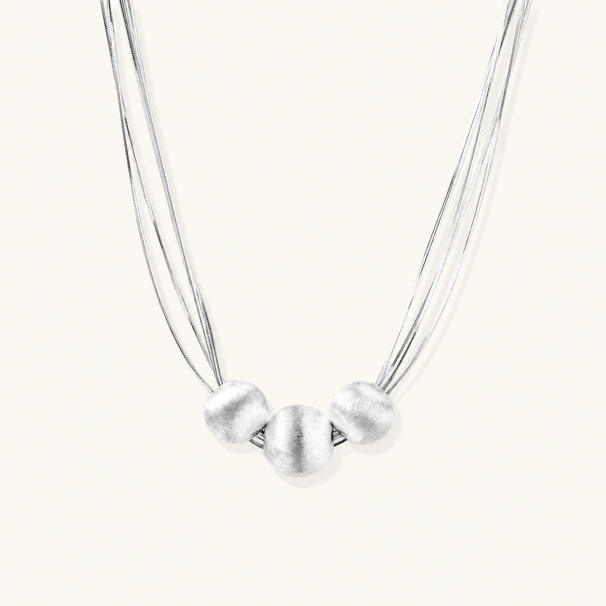 Sterling silver multi-strand necklace with three brushed round beads on cream background