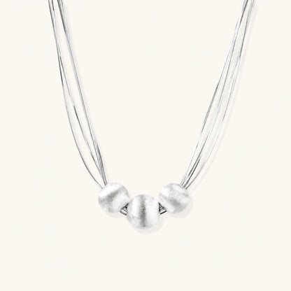 Sterling silver multi-strand necklace with three brushed round beads on cream background