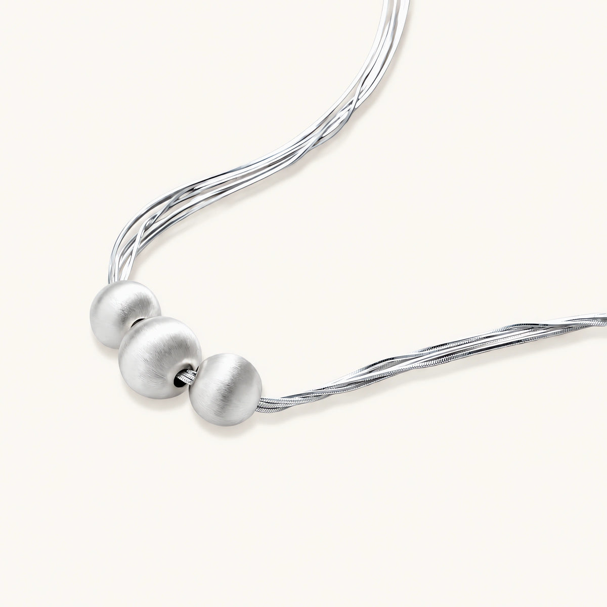 sterling silver multi-strand necklace with three brushed round beads on cream background