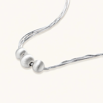 Sterling silver multi-strand necklace with three brushed round beads on cream background
