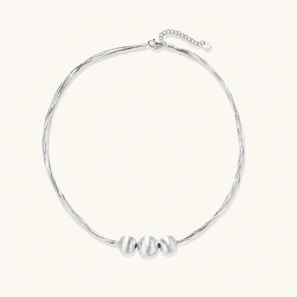 Sterling silver multi-strand necklace with three brushed round beads on cream background