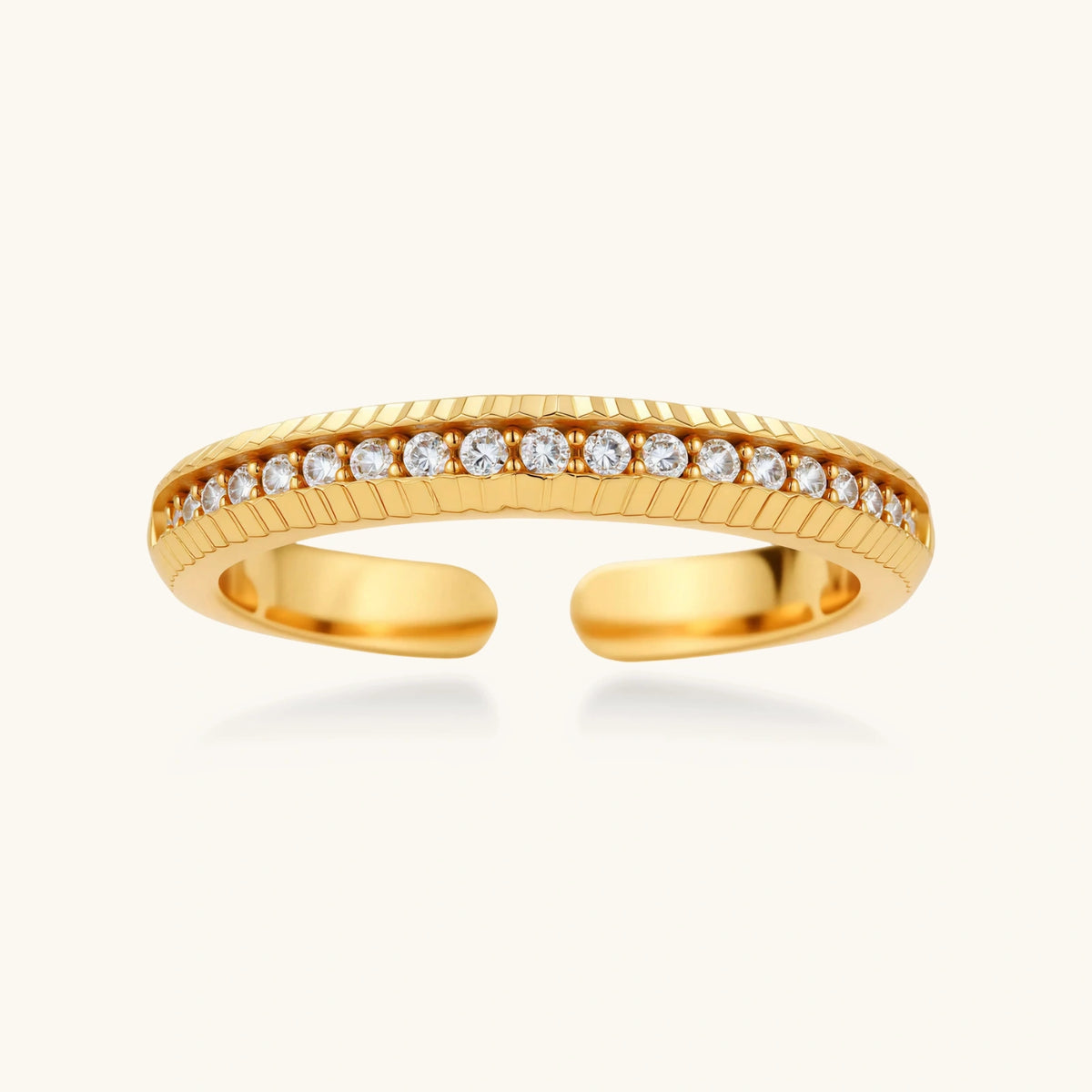 adjustable gold-plated ring with row of sparkling crystals on ribbed band, shot against cream background